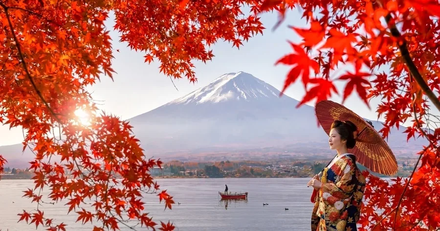 紅葉に縁どられた湖の上の富士山。右側には赤い傘を持った着物姿の女性